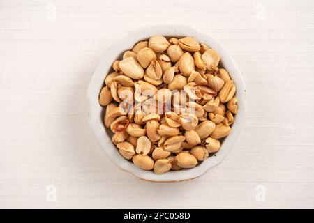 Grains de cacahuètes aromatisés épicés dans un bol sur fond de table blanc. Banque D'Images