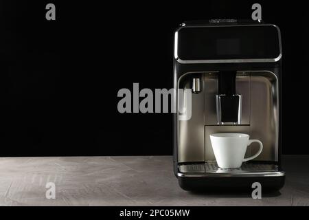 Machine à café moderne avec une tasse sur une table sur fond noir. Espace pour le texte Banque D'Images