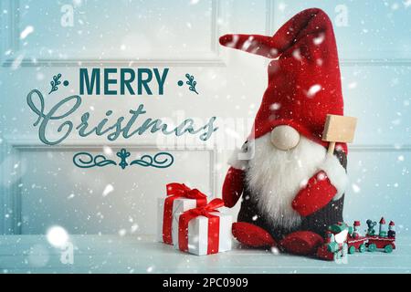 Joyeux Noël ! Gnome mignon, boîtes-cadeaux et train de jouets sur table en bois blanc Banque D'Images