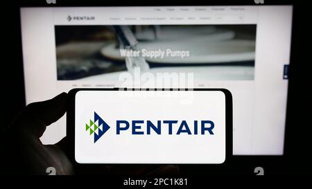 Personne tenant un téléphone portable avec le logo de la société de traitement de l'eau Pentair plc à l'écran en face de la page Web d'affaires. Mise au point sur l'affichage du téléphone. Banque D'Images