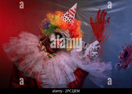 Un clown terrifiant près d'un film de plastique coloré par le sang. Costume de fête d'Halloween Banque D'Images