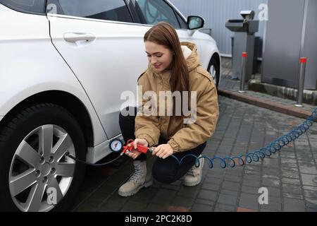 Jeune femme gonflant des pneus au service de voiture Banque D'Images