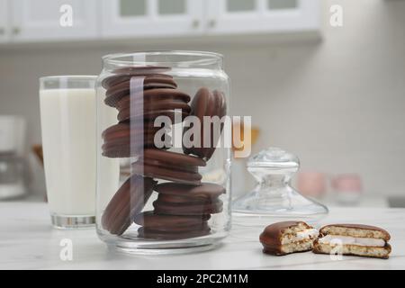 Bol avec de délicieuses tartes au chocolat et un verre de lait sur une table blanche dans la cuisine Banque D'Images