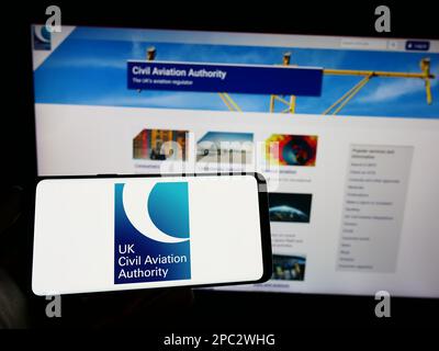 Personne tenant un téléphone portable avec le logo de l'autorité de réglementation britannique de l'aviation civile (CAA) à l'écran devant la page Web. Mise au point sur l'affichage du téléphone. Banque D'Images