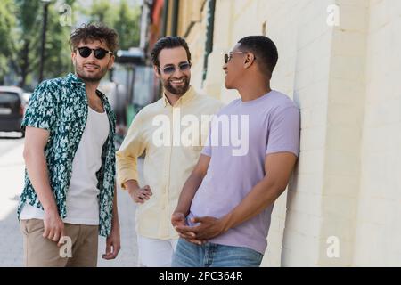 Amis multiethniques positifs dans des lunettes de soleil parlant dans la rue à Kiev, image de stock Banque D'Images