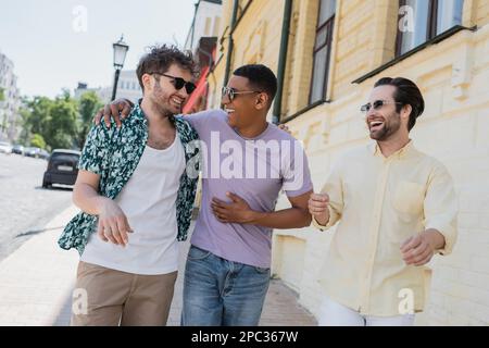 Joyeux amis multiethniques dans des lunettes de soleil marchant sur la descente d'Andrews floue à Kiev, image de stock Banque D'Images