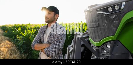 Un agriculteur barbu se trouve devant un tracteur agricole Banque D'Images