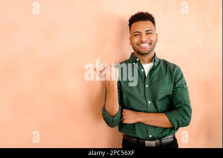 Heureux étudiant indien avec le pouce à part, vendeur indiquant la publicité, recommandant la nouveauté, arabe jeune homme en tenue formelle présentant affaire, promotion, isolé Banque D'Images