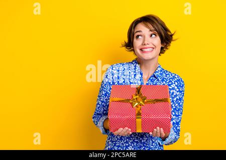 Photo de la drôles rêveuse femme porter chemise d'impression obtenir rouge cadeau paquet regardant vide espace isolé couleur jaune arrière-plan Banque D'Images