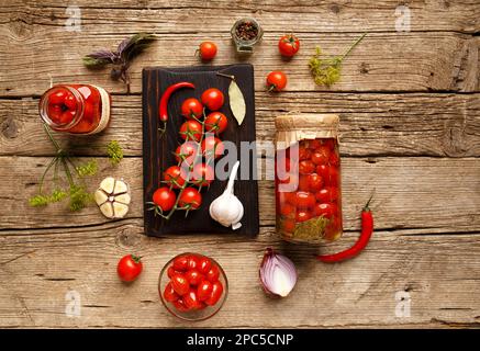 Tomates en conserve dans un pot, branche de cerise, ail, piment, oignon sur un arrière-plan en bois ancien vue du dessus. Ingrédients pour faire mariner les tomates. Banque D'Images