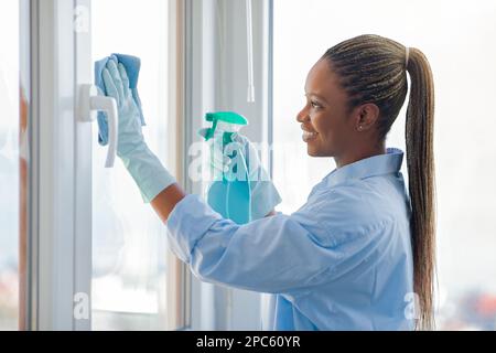 Gaie jeune femme noire femme au foyer nettoyer les fenêtres à la maison Banque D'Images