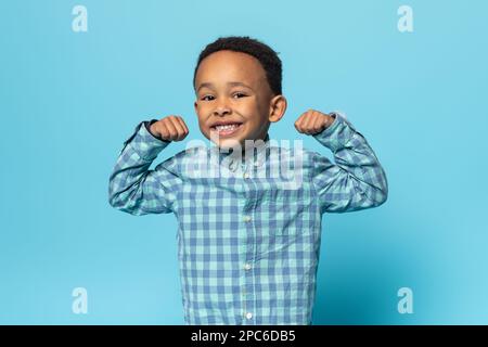 Drôle de garçon noir montrant des biceps et souriant à la caméra, enfant africain américain de sexe masculin démontrant sa puissance et sa force Banque D'Images