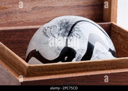 sphère en verre noir et blanc structurée à l'intérieur d'une boîte en bois isolée sur fond blanc Banque D'Images