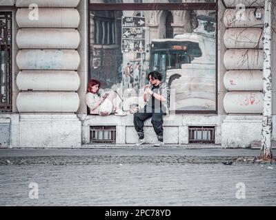 Bucarest, Roumanie - 02.025.2023: Deux jeunes adolescents assis sur le trottoir dans le centre de Bucarest Banque D'Images