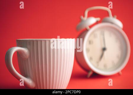 Tasse blanche et réveil sur fond flou. Banque D'Images