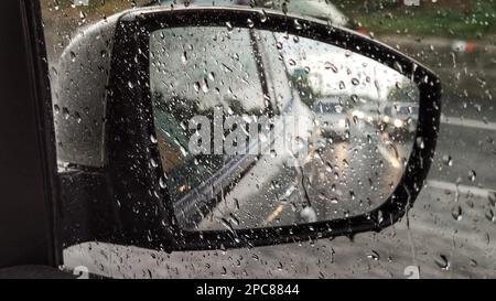 Flou, gouttes de pluie sur une fenêtre de voiture avec le miroir en arrière-plan. Banque D'Images