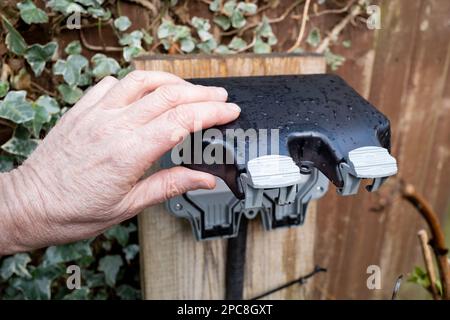 Propriétaire sur le point d'ouvrir le couvercle imperméable d'une double prise électrique externe. Vu dans un jardin après une forte averse Banque D'Images