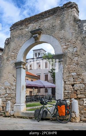 Vélo de tourisme en face des vestiges de l'ancienne porte de la ville romaine dans la ville de Poreč / Parenzo, station balnéaire à la mer Adriatique, Istria Comté, Croatie Banque D'Images