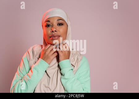 positive multiracial femme en vert manches longues réglage hijab traditionnel isolé sur gris rose, image de stock Banque D'Images