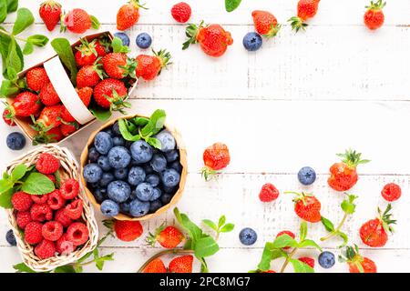 Différentes baies fraîches dans un panier sur fond de bois blanc, vue de dessus.Concept de la cuisine d'été.Flat lay, espace de copie. Banque D'Images