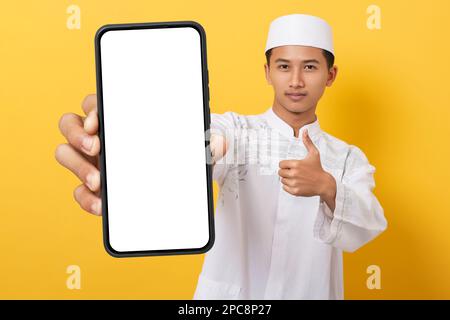 Jeune homme musulman asiatique élégant tenant et montrant un grand smartphone avec écran blanc en main. smartphones mockup pour présentation, application u Banque D'Images