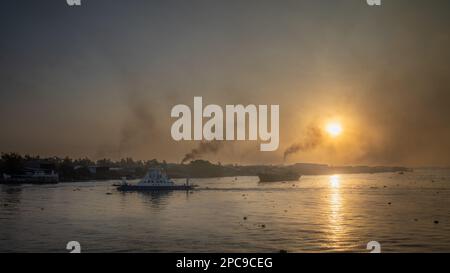 Un ferry traverse le Mékong à l'aube près de long Xuyen dans le delta du Mékong au Vietnam, tandis que la fumée s'élève des fours à briques qui bordent la rive du fleuve. Banque D'Images