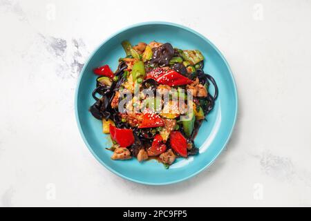 un lagman noir aux champignons de bois, au poulet et au poivre dans une assiette bleue. Banque D'Images