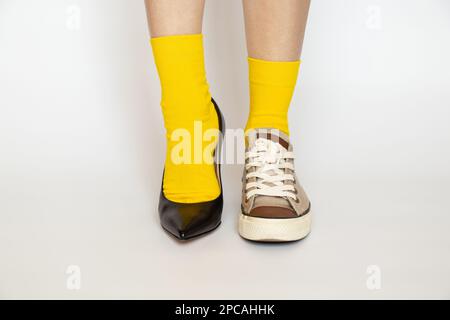 Différentes chaussures sur les jambes de la fille, chaussures à talons hauts et baskets de sport en chaussettes jaunes sur fond blanc, mode Banque D'Images