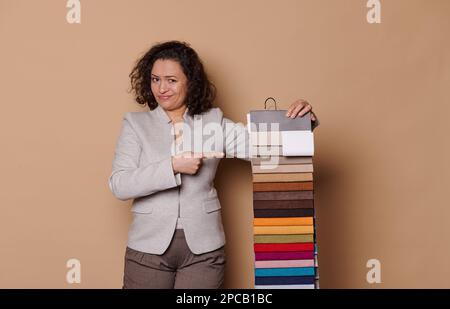 Femme hésitante à poil dur pointant vers des échantillons de tissu, ayant quelques difficultés à choisir des matériaux d'ameublement de canapé Banque D'Images