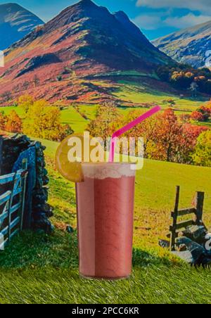 Boisson fouettée aux fruits frais et sains, garnie de crème et d'une tranche de citron, prise sur un paysage de campagne avec des montagnes en arrière-plan. Banque D'Images