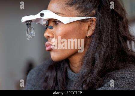 Vue latérale de crop Femme Cosmetologiste noire drôle avec cheveux foncés faire des lèvres pouting portant des lunettes pour microblading dans le salon de beauté Banque D'Images