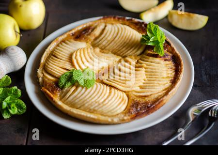 Tarte française aux pommes : tentation sur fond noir. Tarte traditionnelle ouverte avec fines tranches de pommes, décorée de feuilles de menthe. Banque D'Images