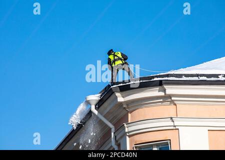 Un homme qui pelait de la neige depuis un toit lors d'une journée d'hiver ensoleillée dans le quartier de Kruununhaka à Helsinki, en Finlande Banque D'Images