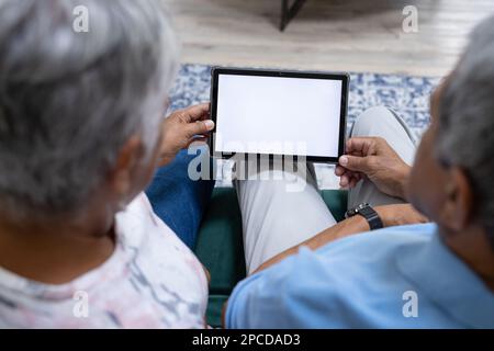 Vue en grand angle d'un couple biracial senior utilisant une tablette numérique tout en se relaxant à la maison, espace de copie Banque D'Images