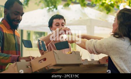 Agricultrice donnant des tranches de pommes gratuites pour les clients au goût, diverses personnes appréciant le produit samplingg sur le marché alimentaire. Jeune femme donnant des échantillons de produits biologiques aux cuspières. Prise de vue à main levée. Banque D'Images