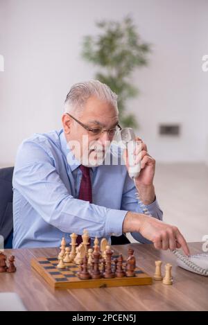 Un vieil employé de sexe masculin joue aux échecs dans le bureau Banque D'Images