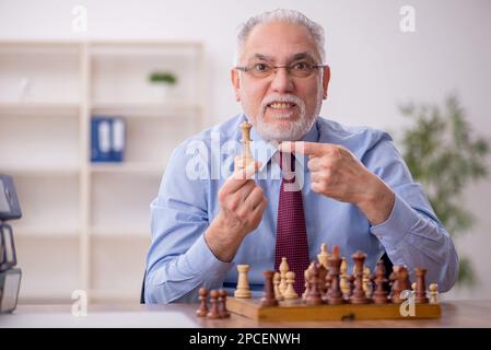 Un vieil employé de sexe masculin joue aux échecs dans le bureau Banque D'Images