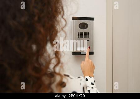 Femme afro-américaine sonnant intercom avec caméra dans l'entrée, gros plan Banque D'Images