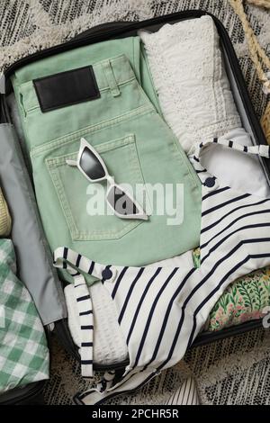 Valise ouverte avec vêtements d'été et lunettes de soleil sur le sol, vue du dessus Banque D'Images