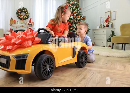 Mignon petit garçon poussant la voiture jouet avec sa sœur dans la chambre décorée pour Noël Banque D'Images