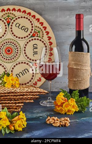 Pesach célébration concept - vacances juives Pesach. Fond avec fleurs jaunes avec verre de vin, matzah et assiette de séder sur fond bleu Banque D'Images