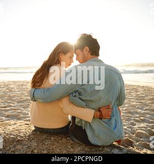 Ils ont trouvé un endroit romantique sur la plage. Vue arrière d'un jeune couple aimant assis les uns à côté des autres sur un rocher à la plage. Banque D'Images