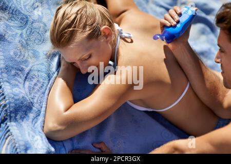 Amusez-vous avec la crème solaire. Un jeune couple appliquant de la crème solaire à la plage. Banque D'Images