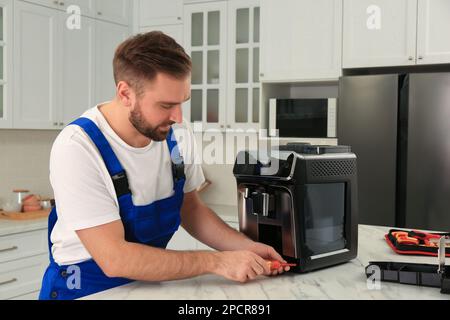 Réparateur avec tournevis fixant la machine à café à la table dans la cuisine Banque D'Images