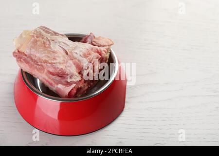Bol d'alimentation avec os de viande hachés crus sur une table en bois blanc. Espace pour le texte Banque D'Images