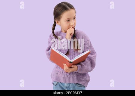 Petite fille avec livre mordant des ongles sur fond lilas Banque D'Images