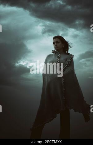 Belle jeune femme portant un châle debout contre un ciel sombre Banque D'Images