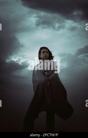 Belle jeune femme portant un châle debout contre un ciel sombre Banque D'Images