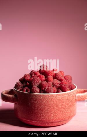 Framboises verticales dans un bol en argile sur fond rose. Banque D'Images