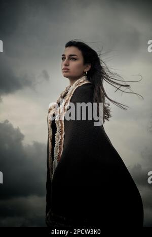 Belle jeune femme portant un châle debout contre un ciel sombre Banque D'Images